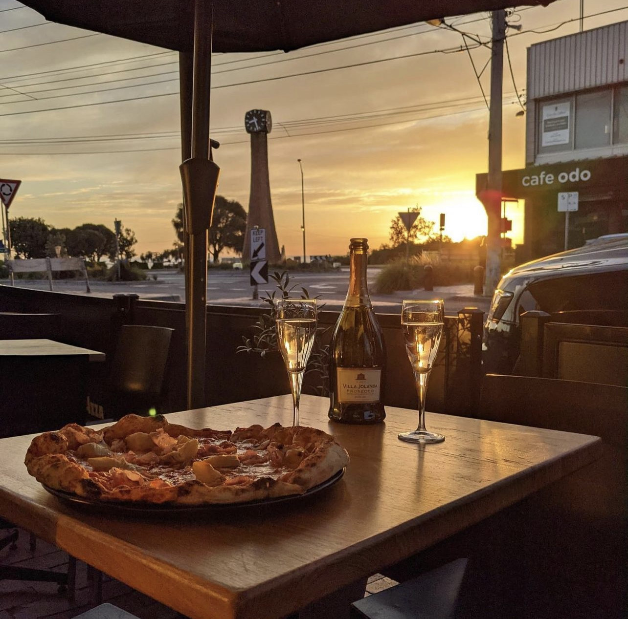 Pizza and a bottle of prosecco on the outdoor table at sunset, with the Black Rock clock tower across the road